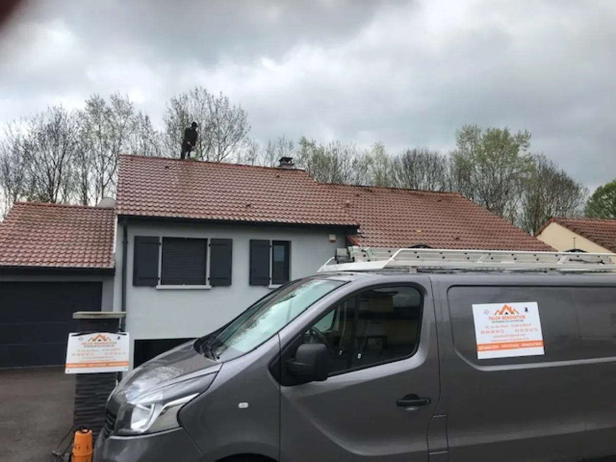 Camionnette de chantier garée devant une maison, un couvreur sur le toit
