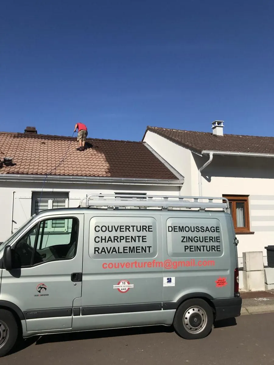 Camion de Falck Rénovation devant un chantier, un couvreur sur le toit