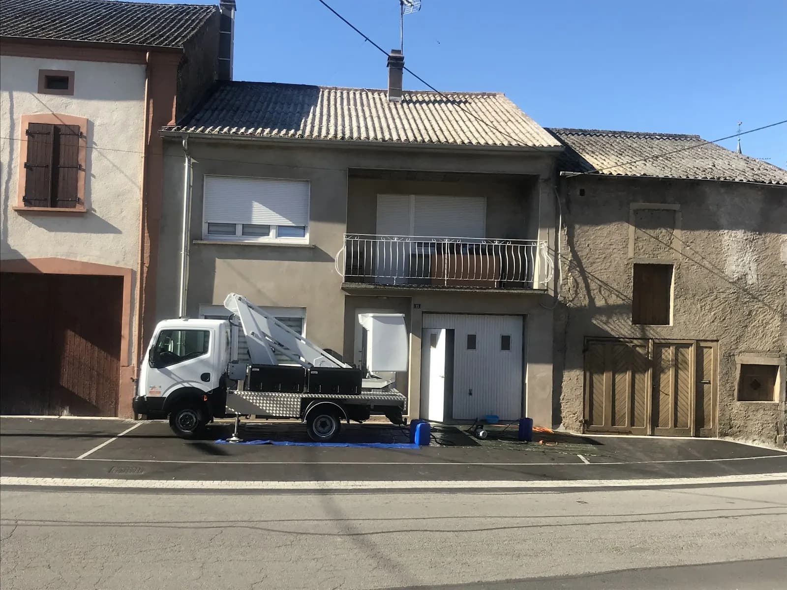 Camion nacelle garé devant des maisons de village, bâche au sol