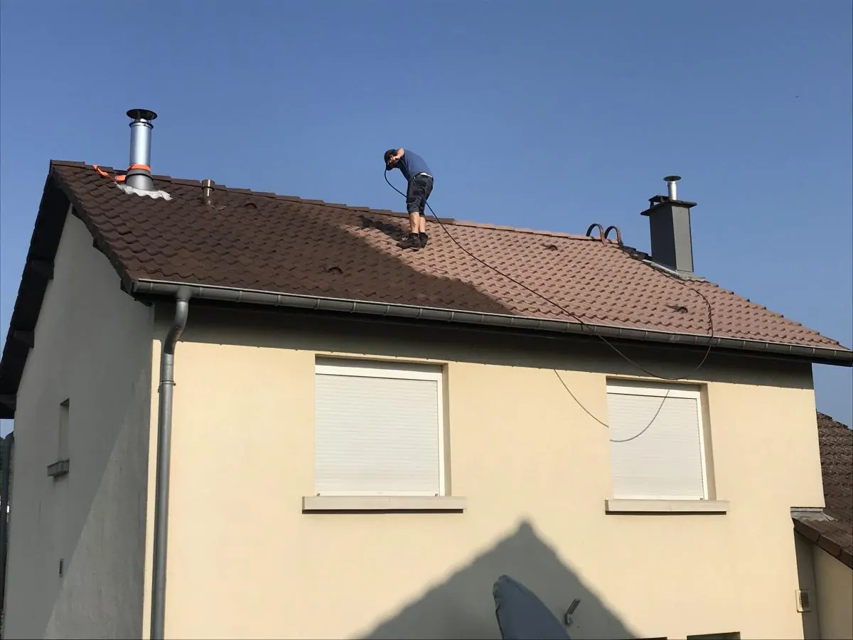 Couvreur debout sur la toiture en tuiles brunes d’un pavillon