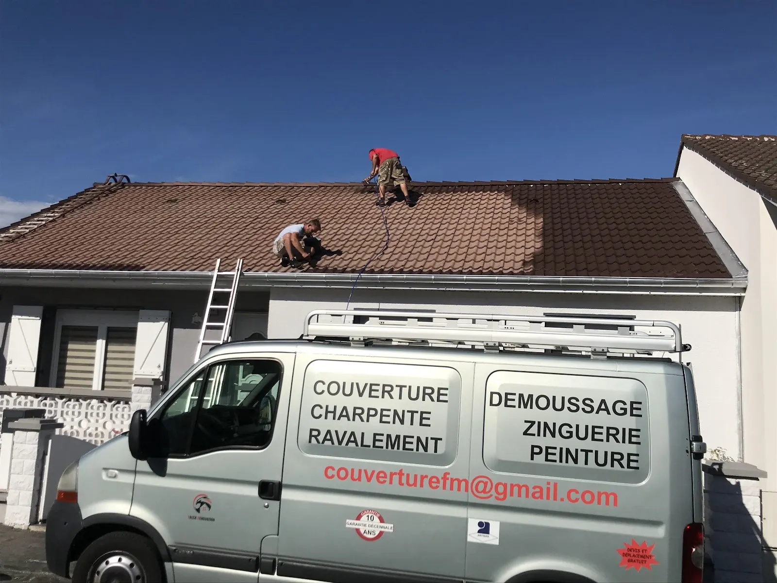 Deux couvreurs sur une toiture en tuiles brunes, la camionnette de l’entreprise garée devant